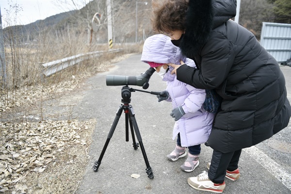할머니가 손녀가 독수리를 관찰할 수 있도록 필드스코프를 보도록 도와주고 있다. 