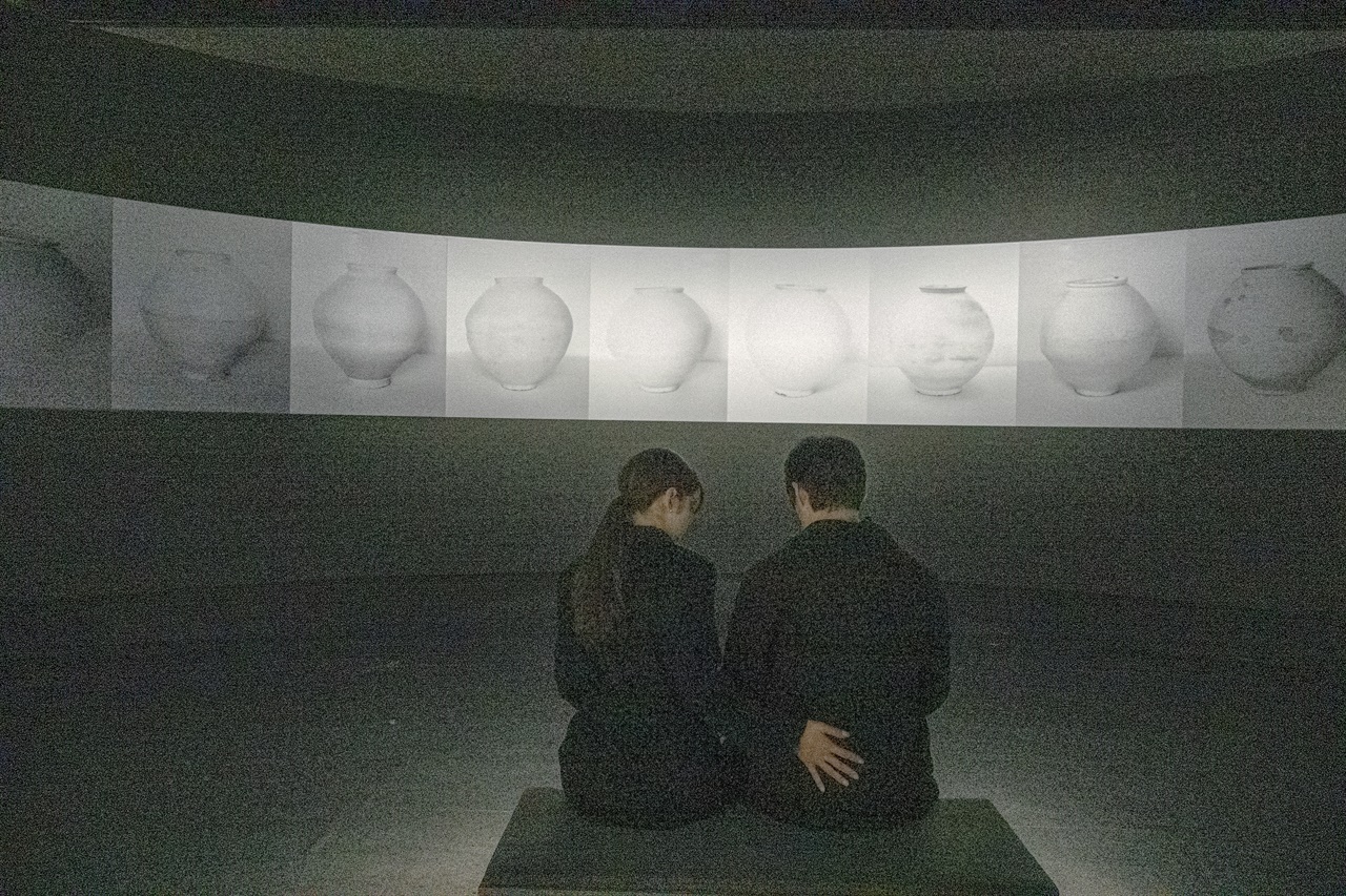  12개의 달항아리를 찍은 '문라이징Ⅲ' 앞에서 한 쌍의 연인이 달빛이 비추듯 다정하게 앉아 있다.