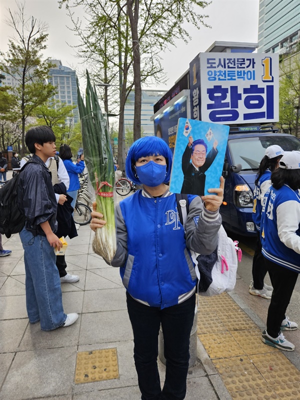 민주당의 상징 색깔인 파란색 점퍼에 파란색 가발을 쓴 한 시민이 대파를 들어보인다.
