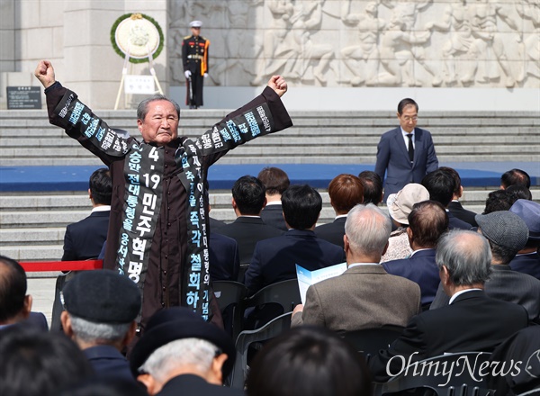 19일 오전 서울 강북구 국립4.19민주묘지에서 열린 ‘제63주년  4.19혁명 기념식’에서 한덕수 총리가 기념사를 하는 동안, 한 참석자가 자리에서 일어나 ‘독재자 이승만 기념관 건립 반대’ 시위를 벌이고 있다.