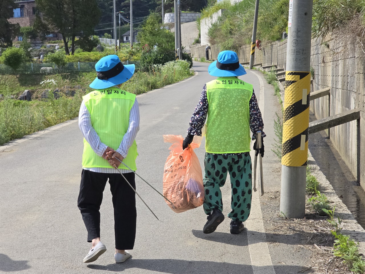 어르신들이 마을회관까지 도보로 걸어간다. 2인 1조로 하루 3시간 동안 저수지부터 마을회관까지  안전하게 청소를 하고 있다.