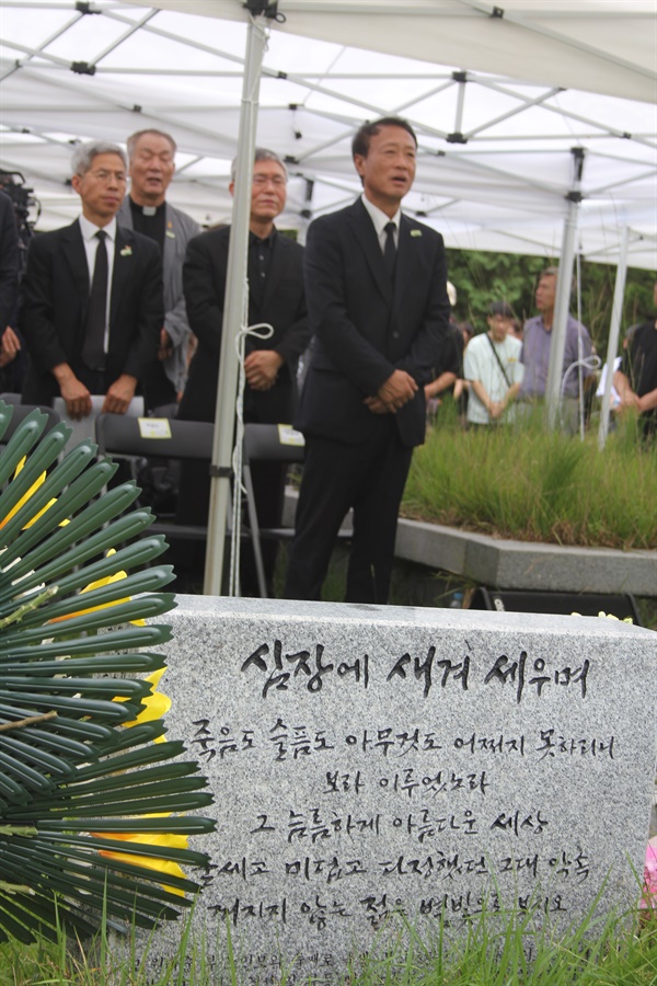 노회찬의 묘비 후면 노회찬 묘비의 뒤로 조승수 노회찬재단 이사장의 모습이 보인다. 묘비의 후면에는 '심장에 새겨 세우며'란 글이 써있다.