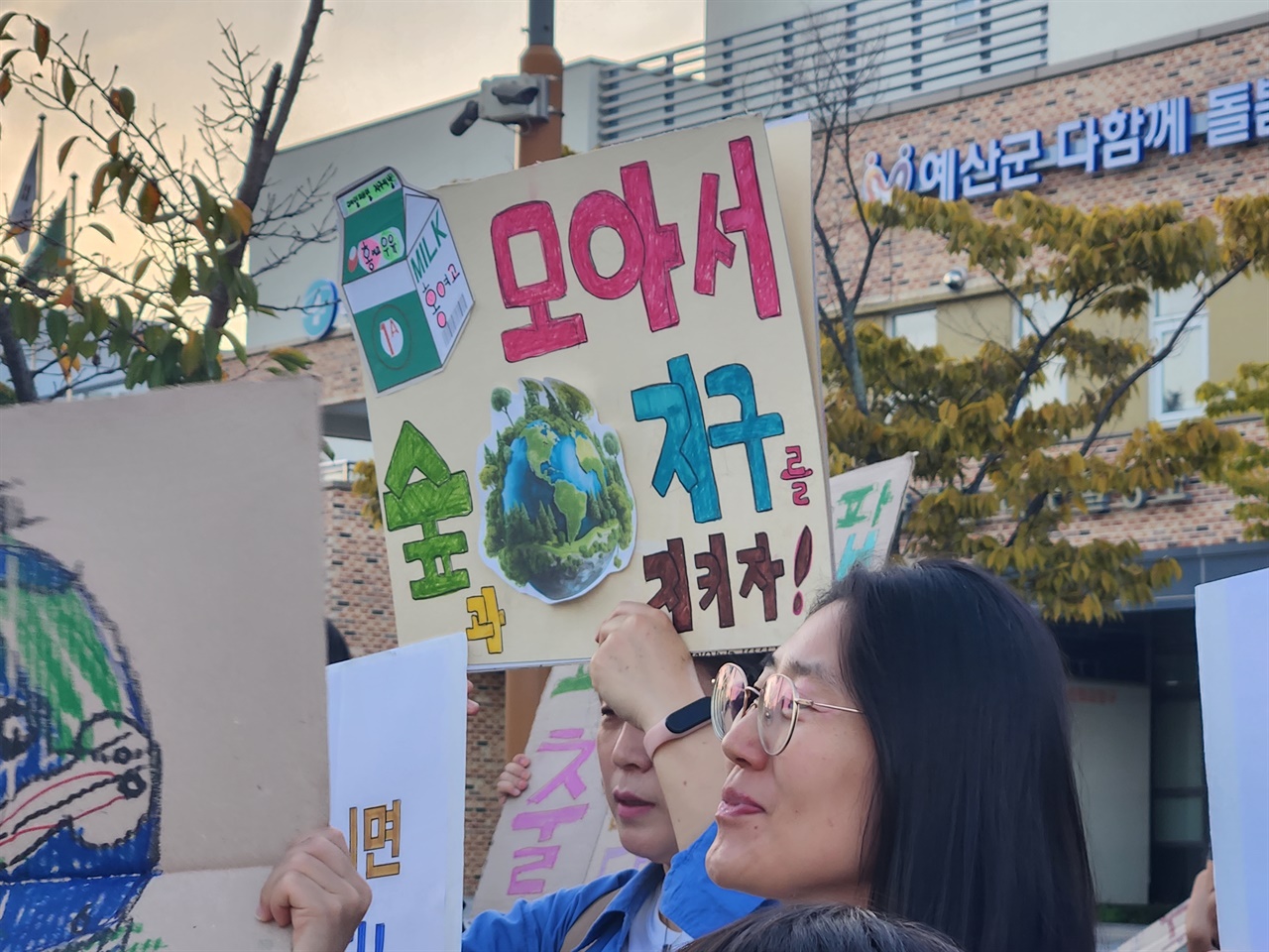  어느 시민이 '우유팩 모아서 지구를 숲과 지구를 지키자'는 메시지가 담긴 피켓을 들고 있다.