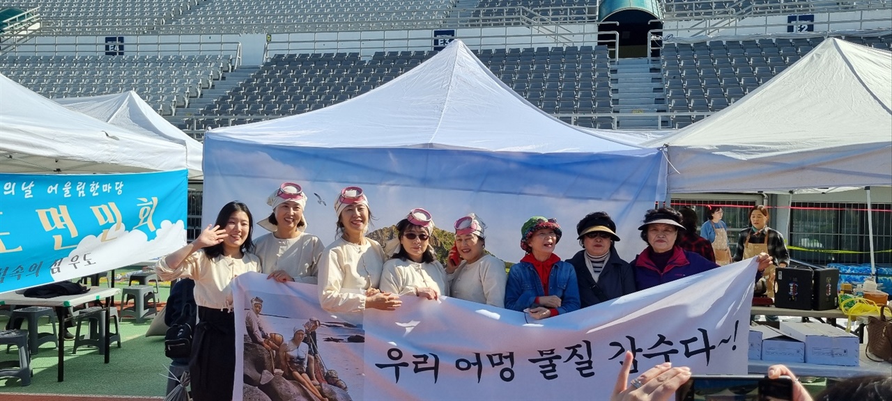 우리어멍 물질 감수다 ‘우리어멍 물질 감수다’해녀체험관 현수막을 배경으로 인증샷을 찍는 서울성산읍민회 팀