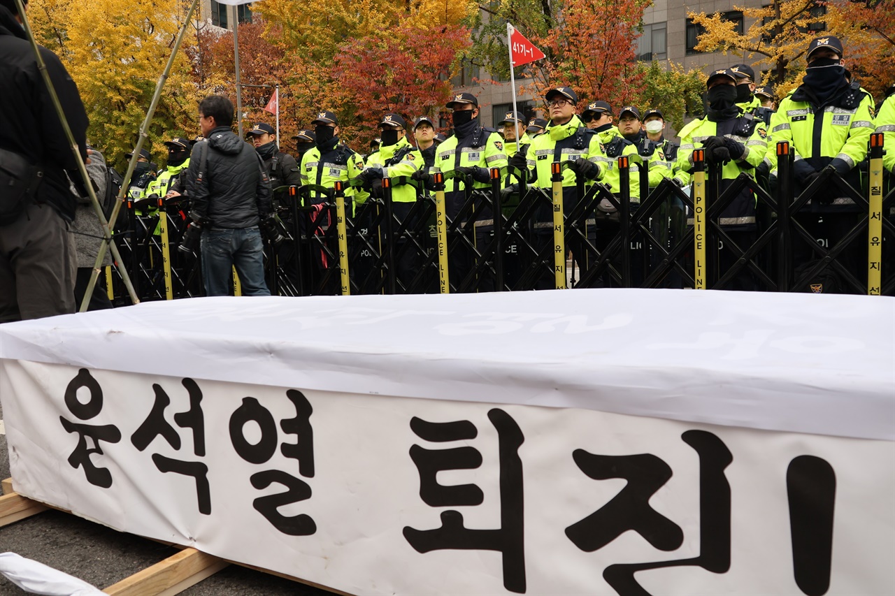  도로를 통제하는 경찰들의 앞에 윤석열 정부의 퇴진을 촉구하는 문구가 적힌 관이 놓여있다.