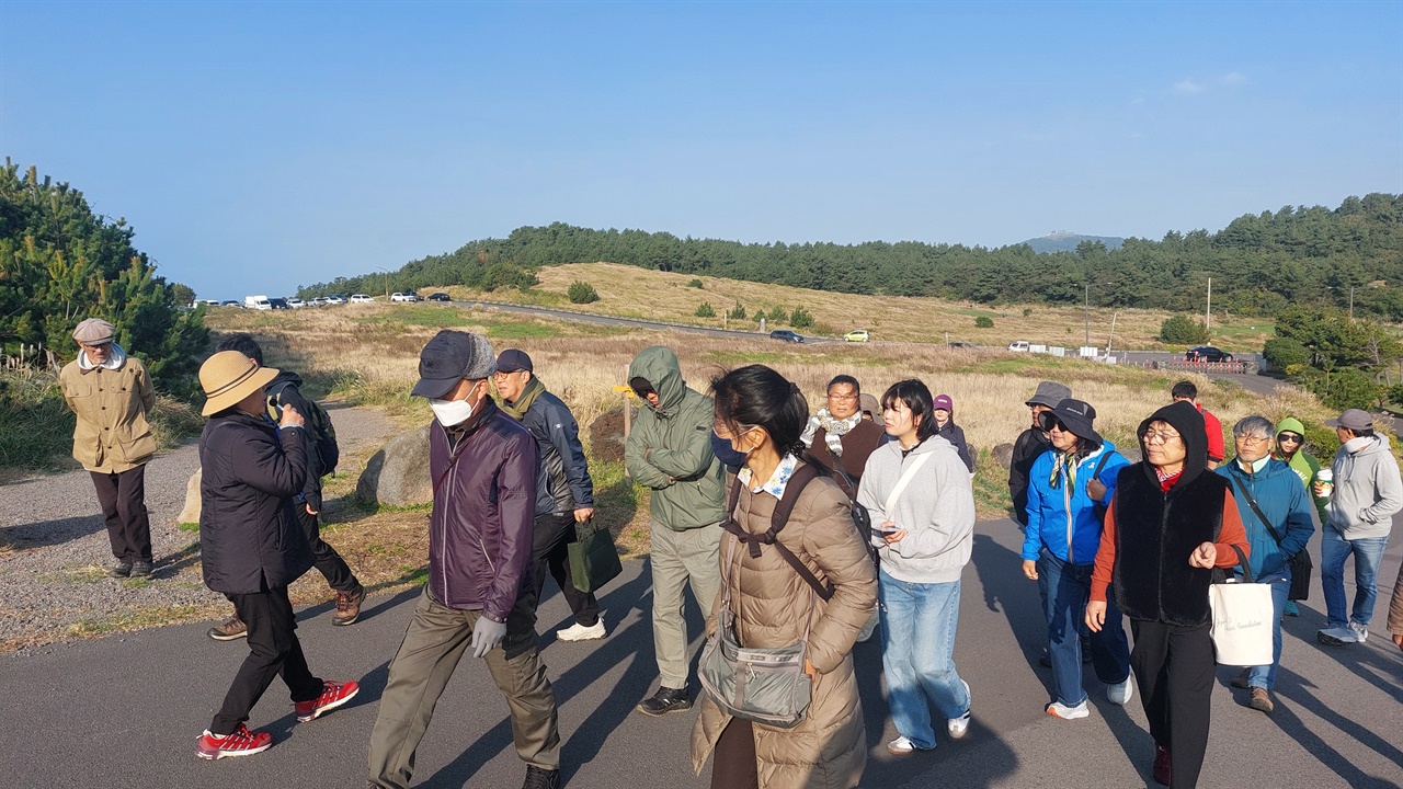  다른제주연구소 회원들과 송악산알뜨르사람들이 김정임 대표의 해설을 들으며 송악산에 오르고 있다. 뒷배경이 종합스포츠타운 예정지.